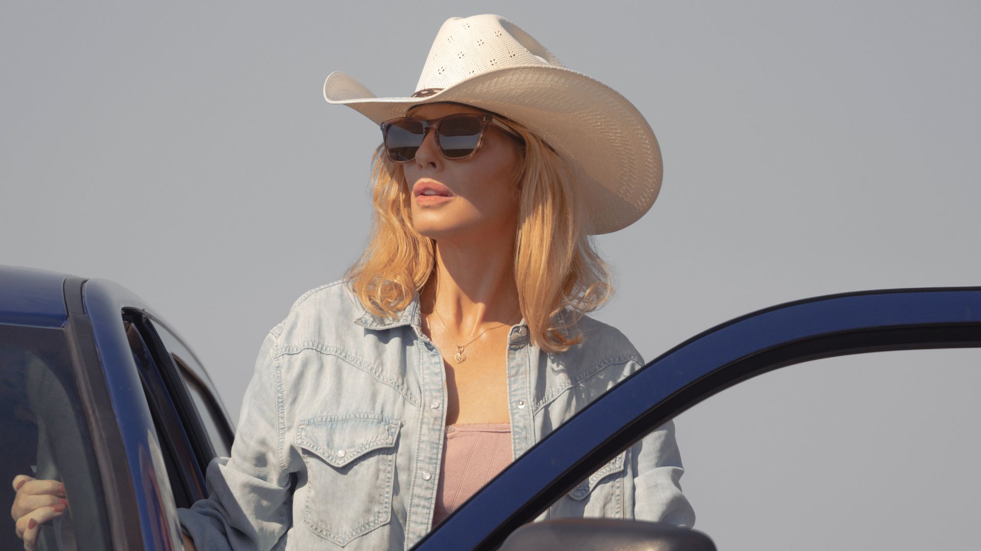 Beth Dutton looks on while standing behind an open car door