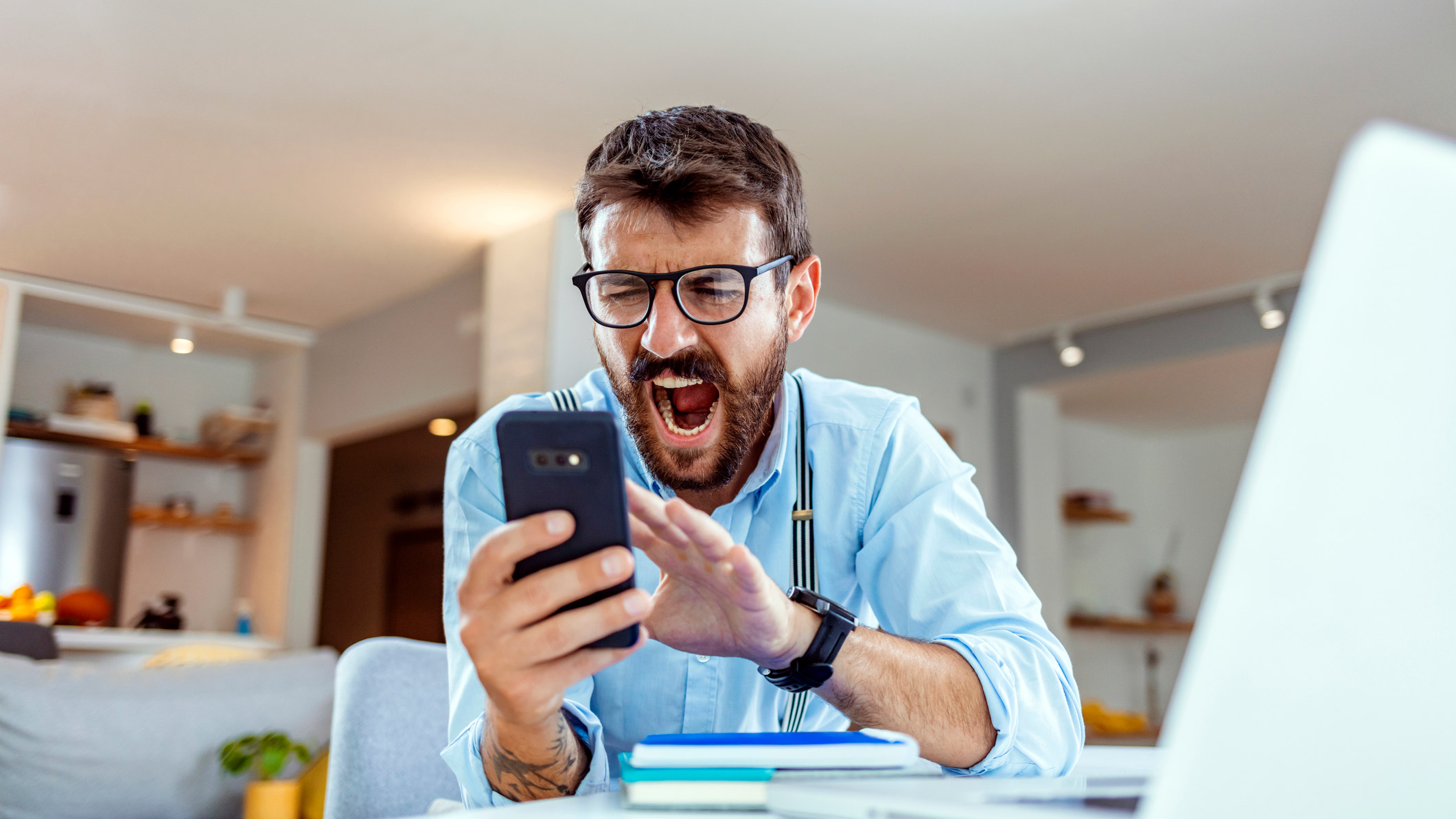 Angry man shouting at mobile phone while sitting at a desk