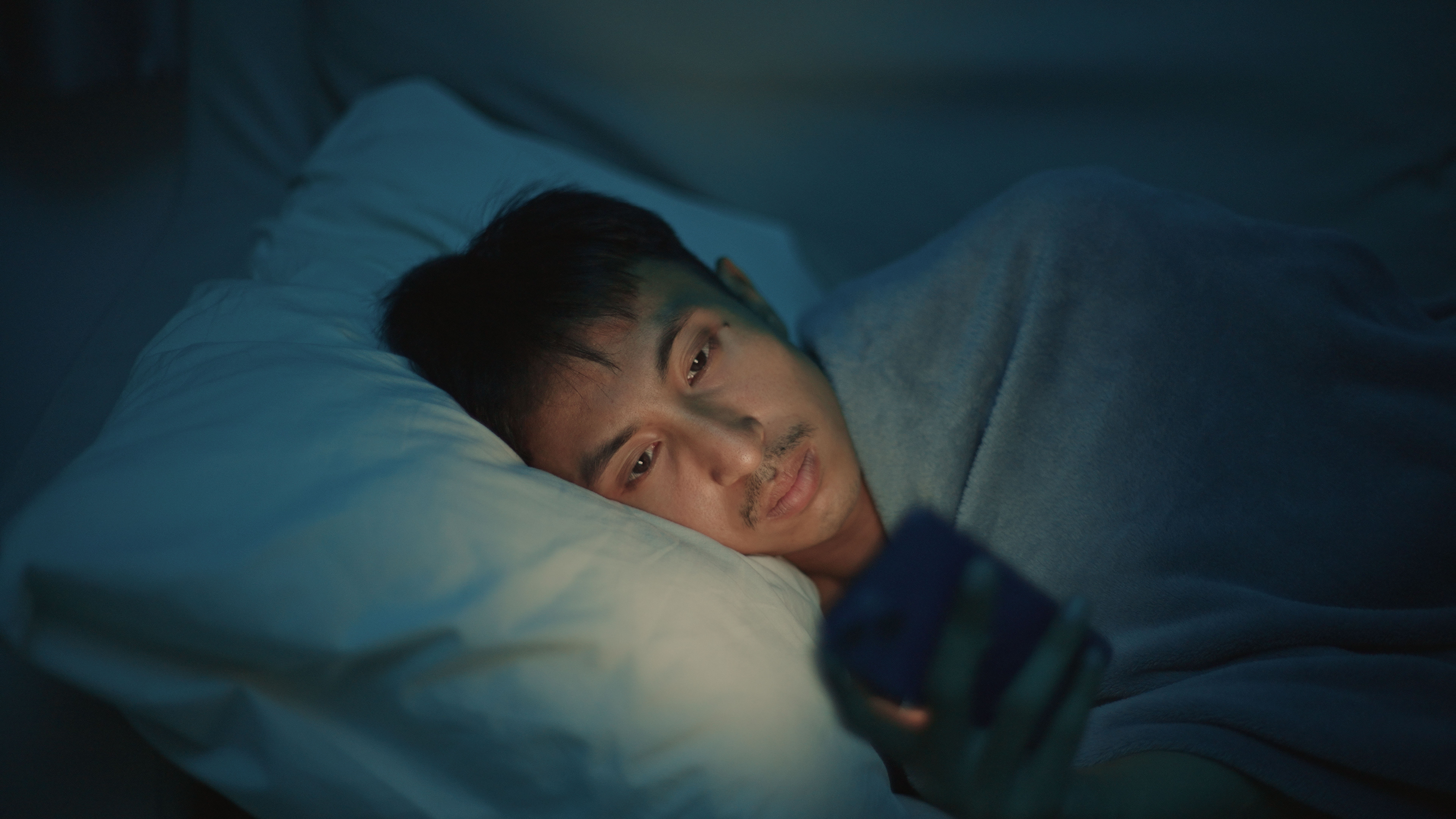 Asian man using smartphone on bed at night, insomnia and social media addiction.