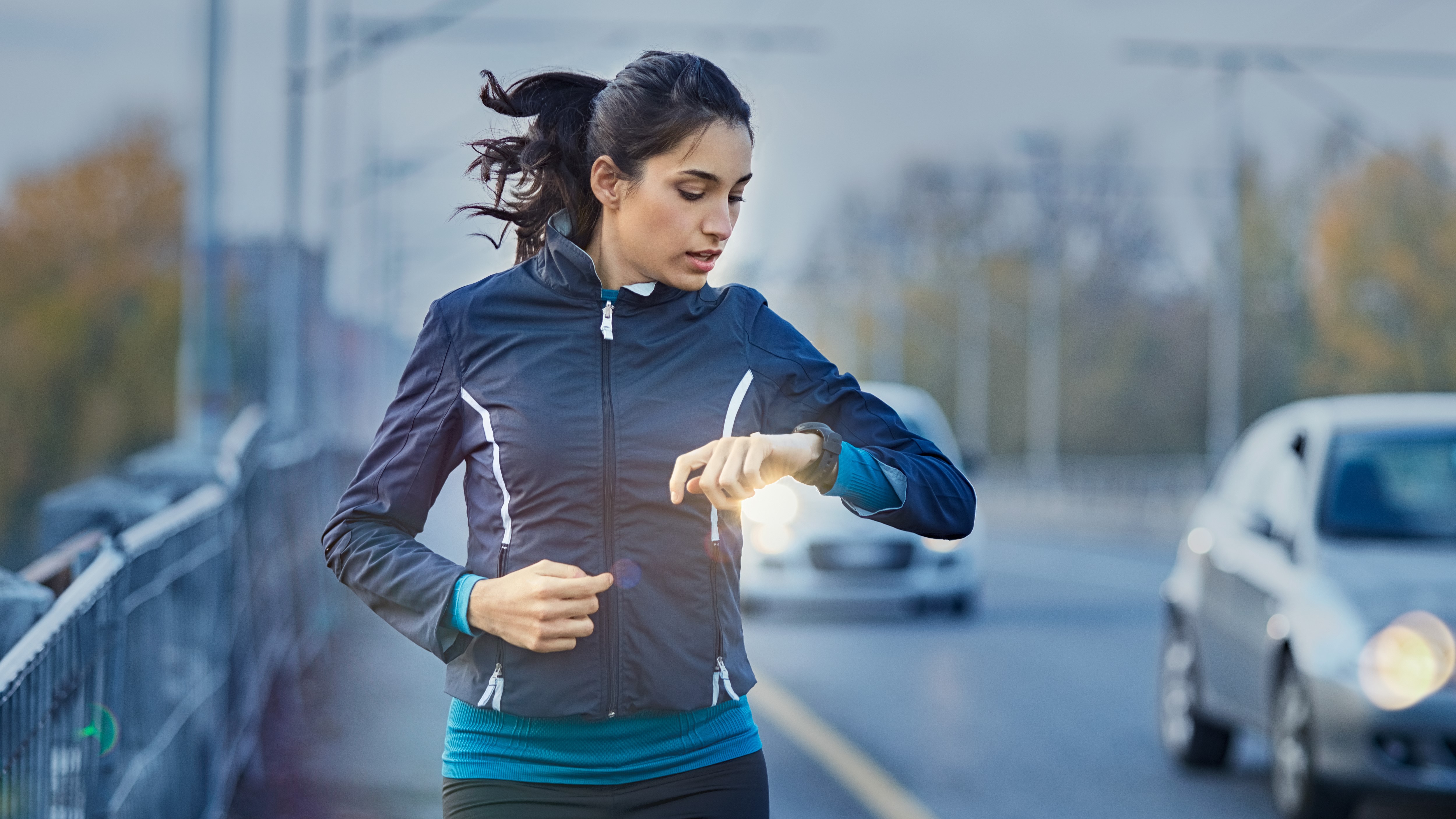 Woman running by a road, checking her running watch