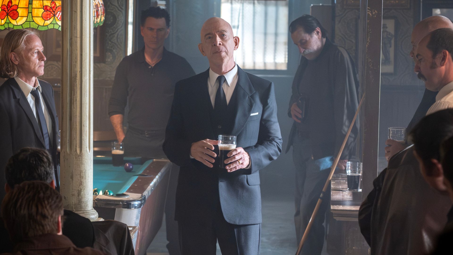 Eammon stands in the center of a pub holding a pint