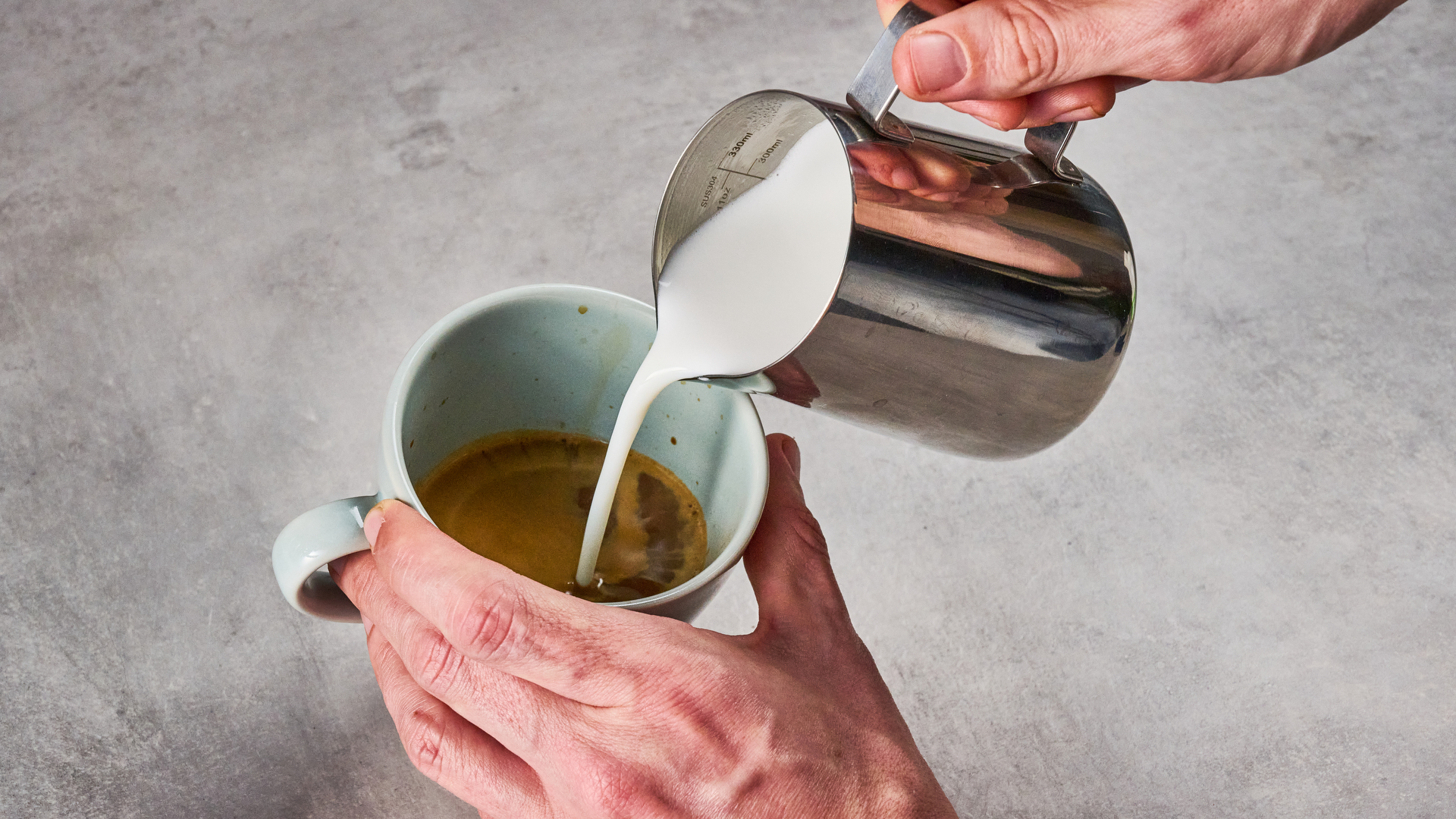 A man pours foamed milk into a double espresso.