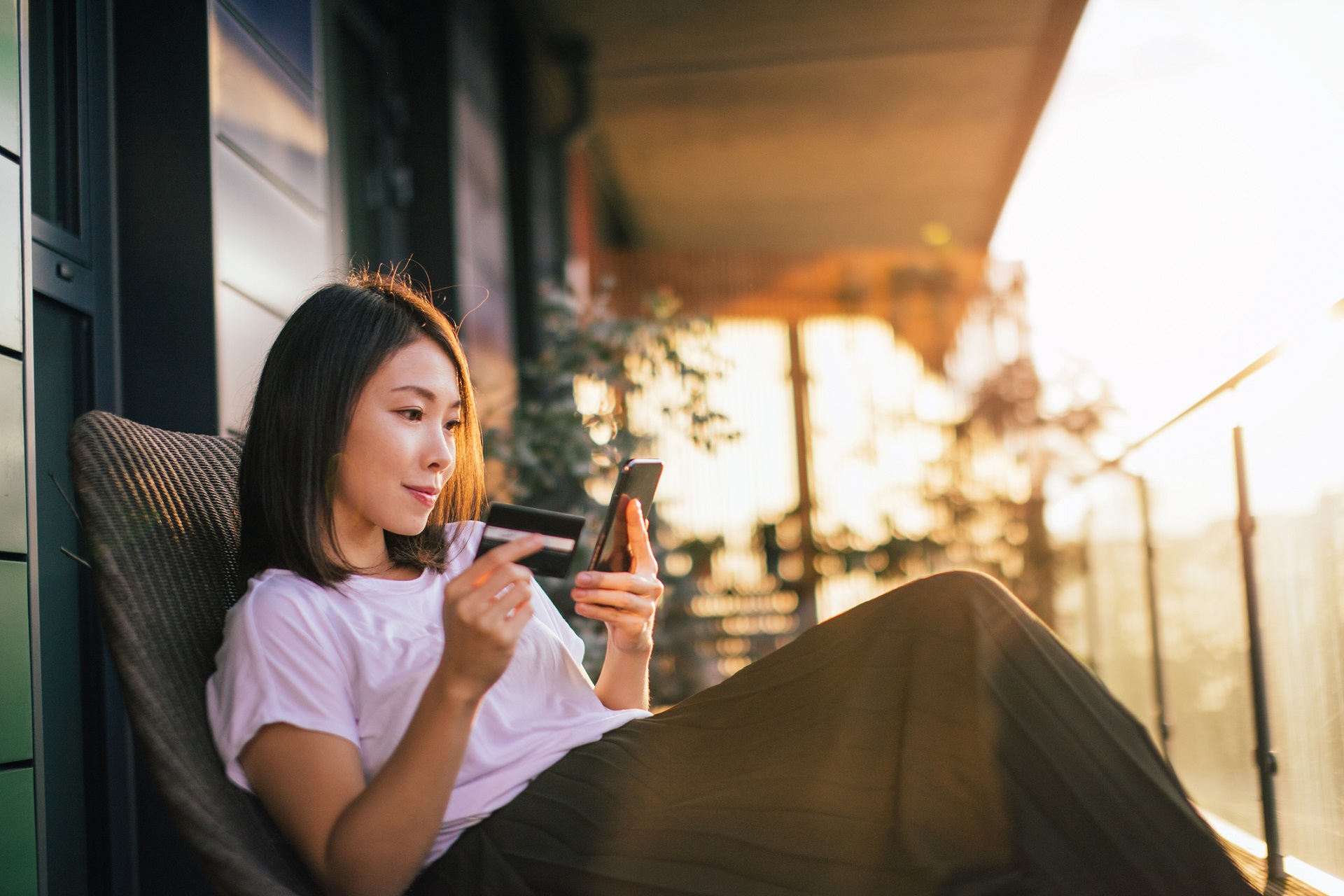 Woman sat on porch using credit card and phone at sunset
