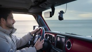 70mai Omni 4K dash cam attached to windscreen of a car with driver on the road, ocean backdrop