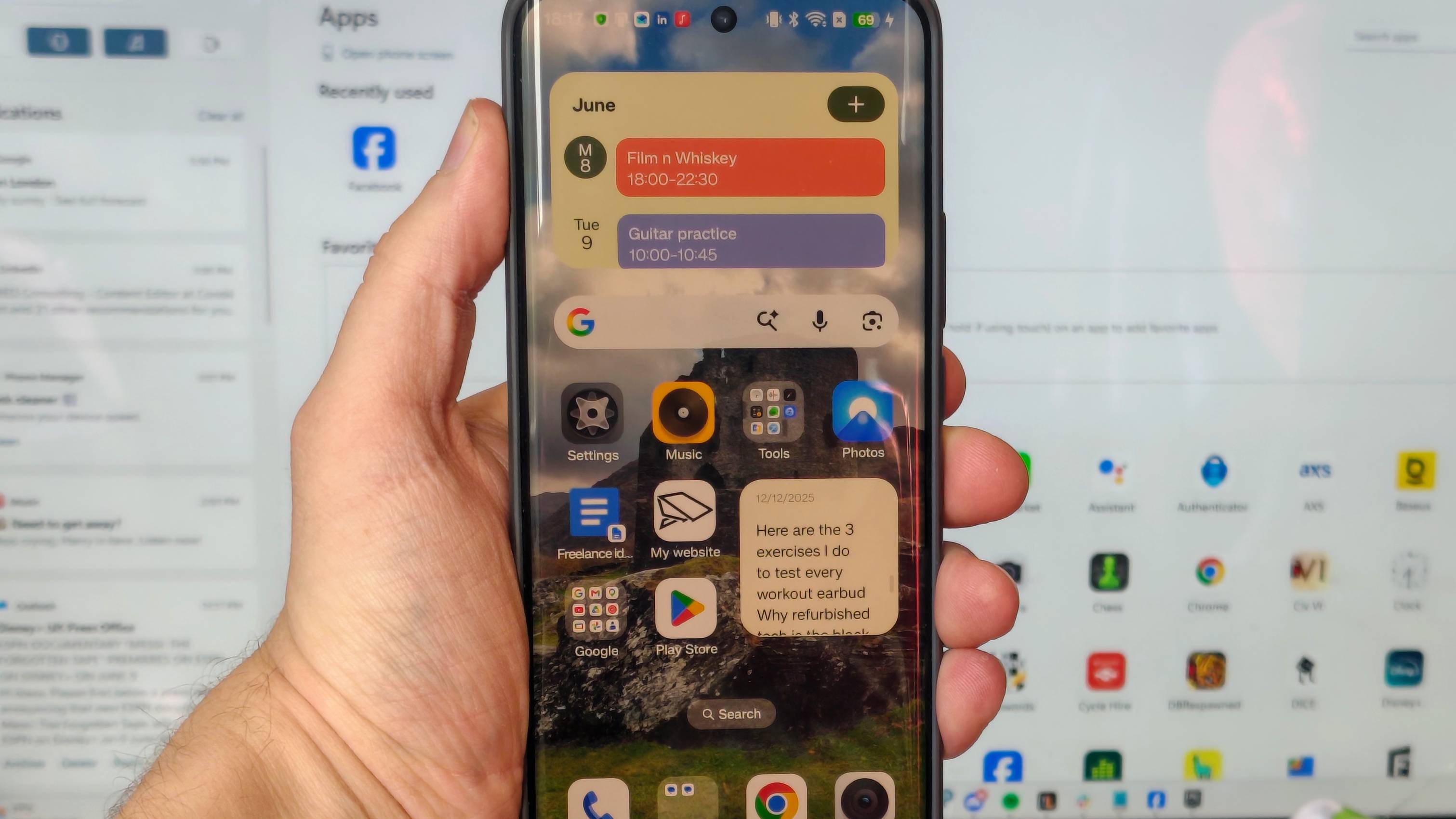An Android phone, being held in front of a PC screen showing Phone Link.