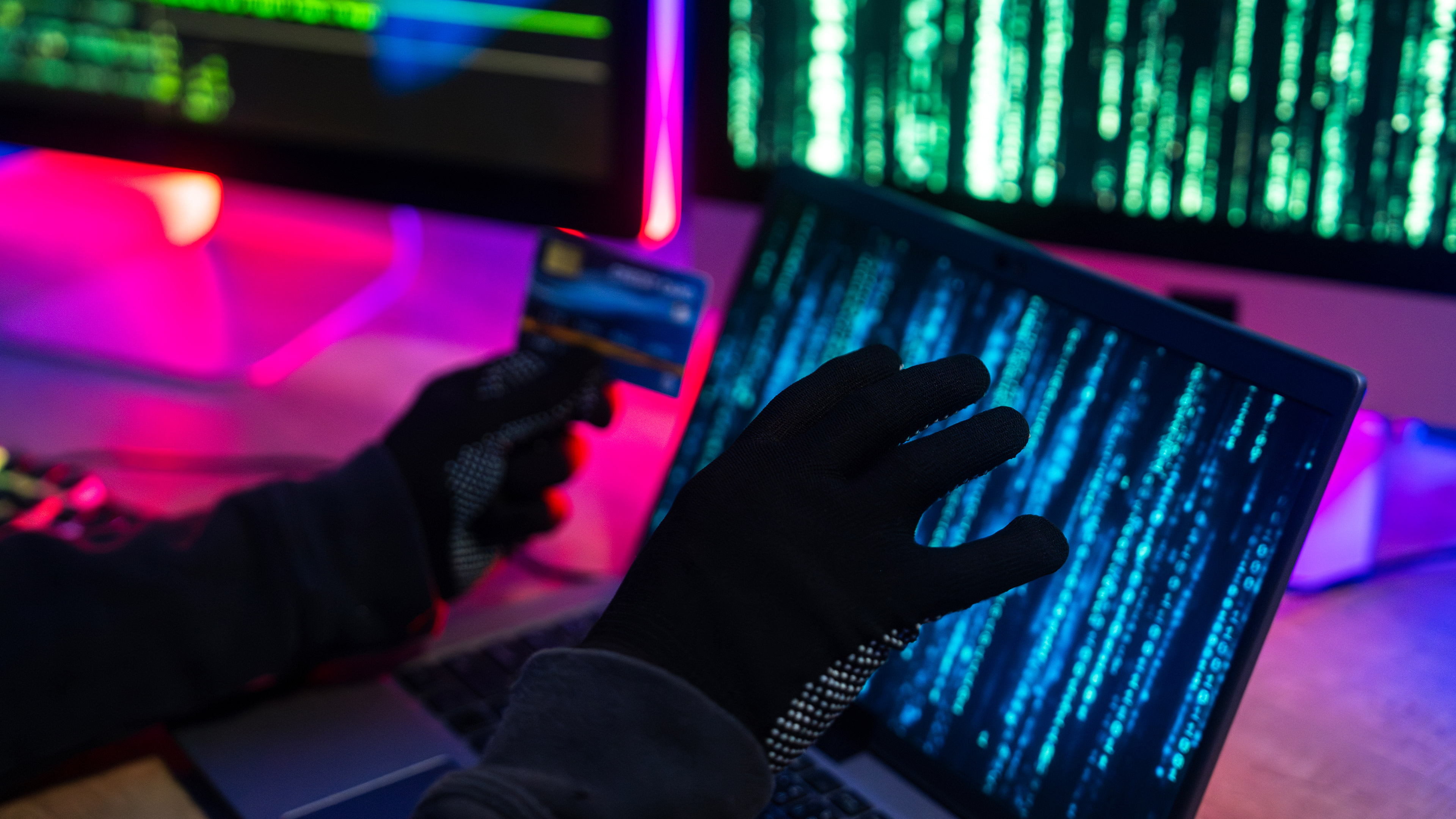A hand holding a credit card in front of a laptop screen with Matrix-style data on it