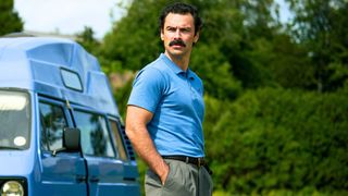 Declan looks at something off screen standing in front of a minivan