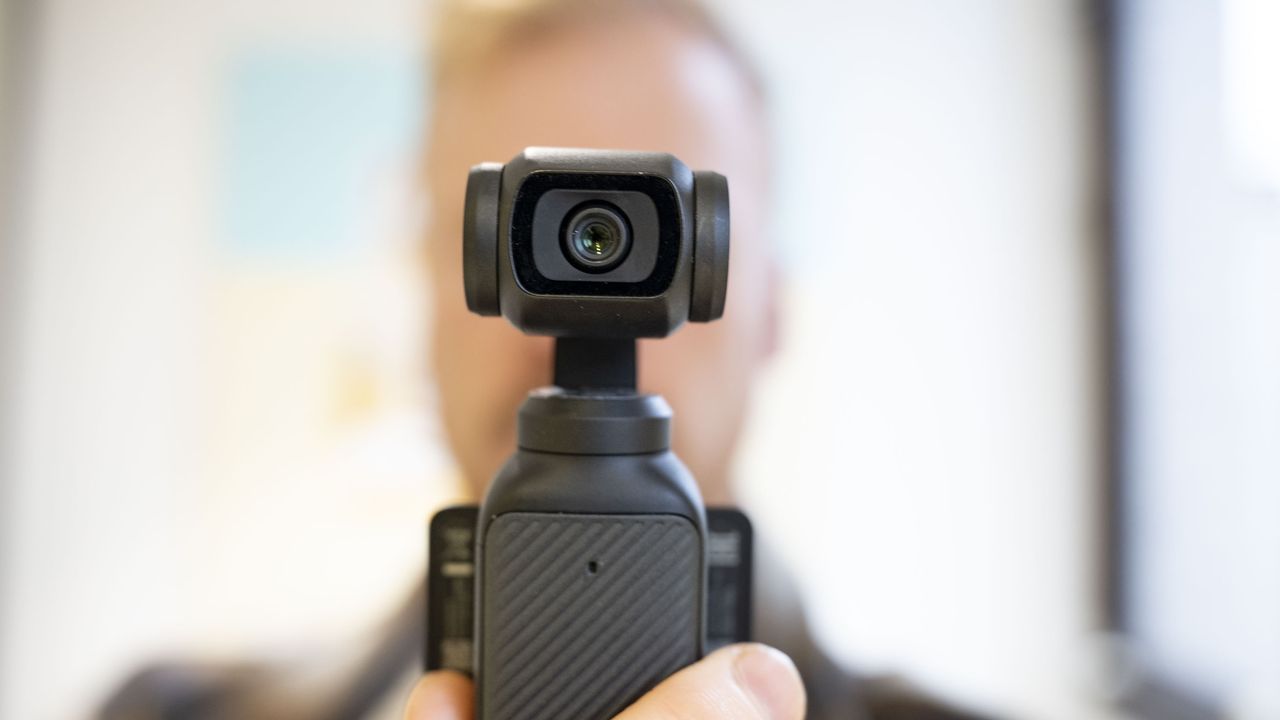 DJI Osmo Pocket 3 vlogging camera in usr's hand, with them blurred in the background