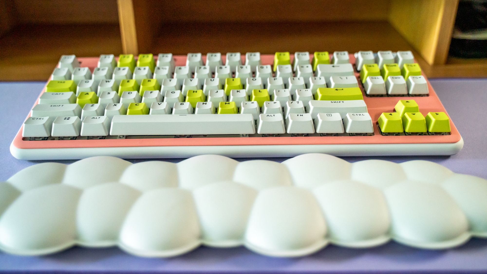 Logitech G715 TKL in its pink deck cover and white and green keys on purple Logitech desk mat