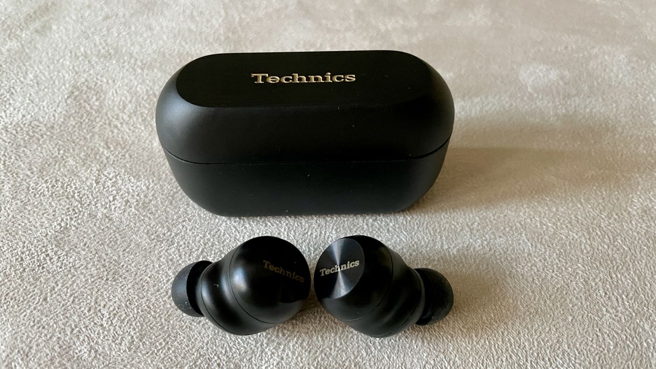 Technics EAH-AZ100 earbuds in black, on a beige background, held in a hand