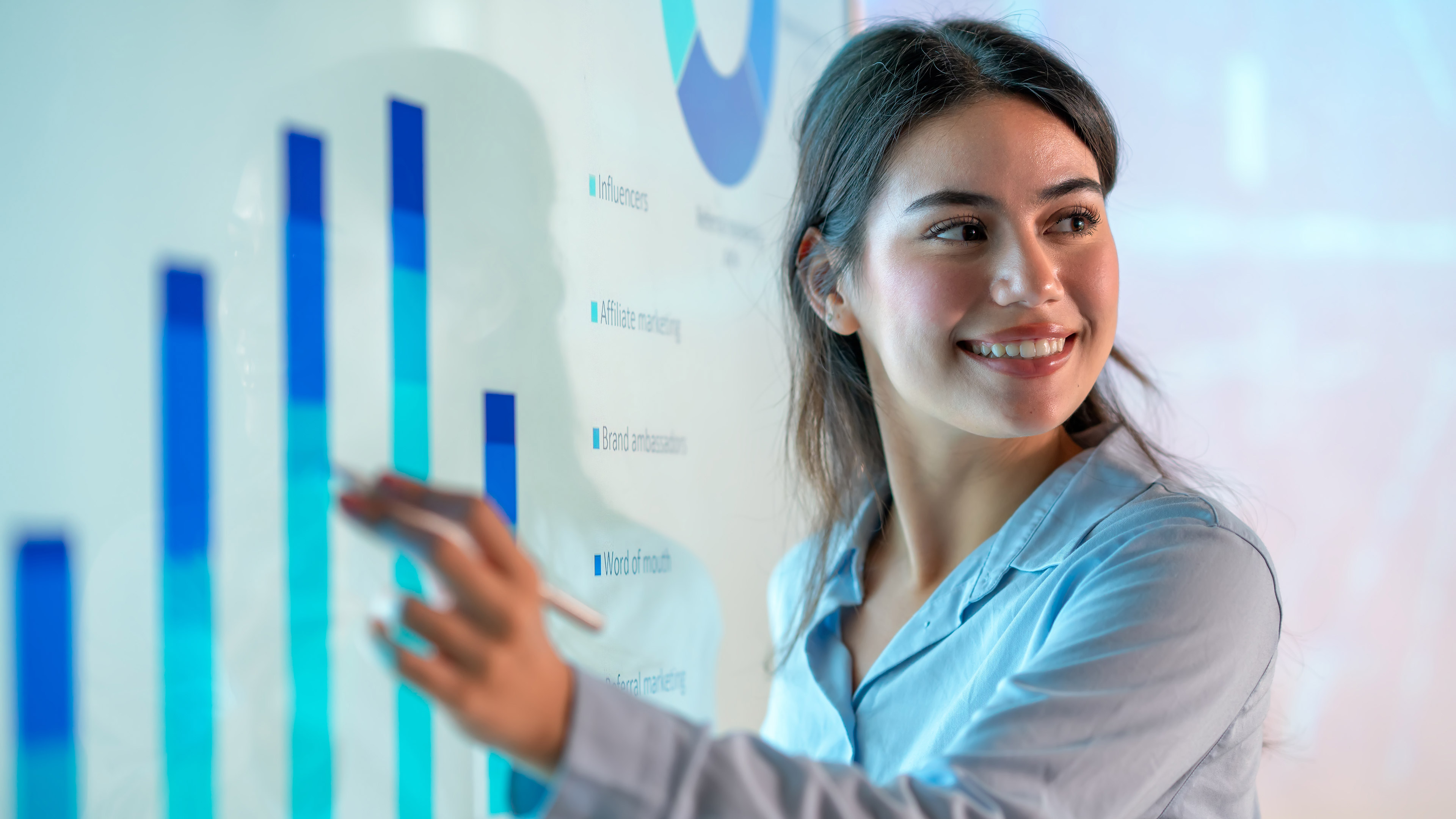 A female office worker smiling as she presents data on a giant display