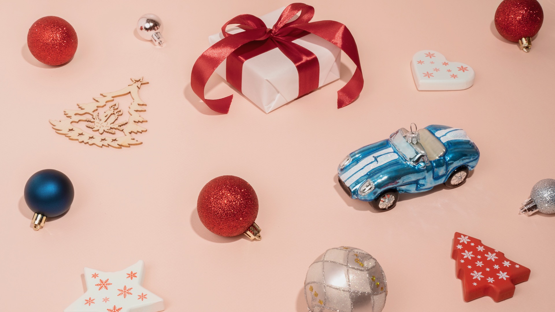 A pink paper background with Christmas baubles and Christmas tree decorations laid out on it.