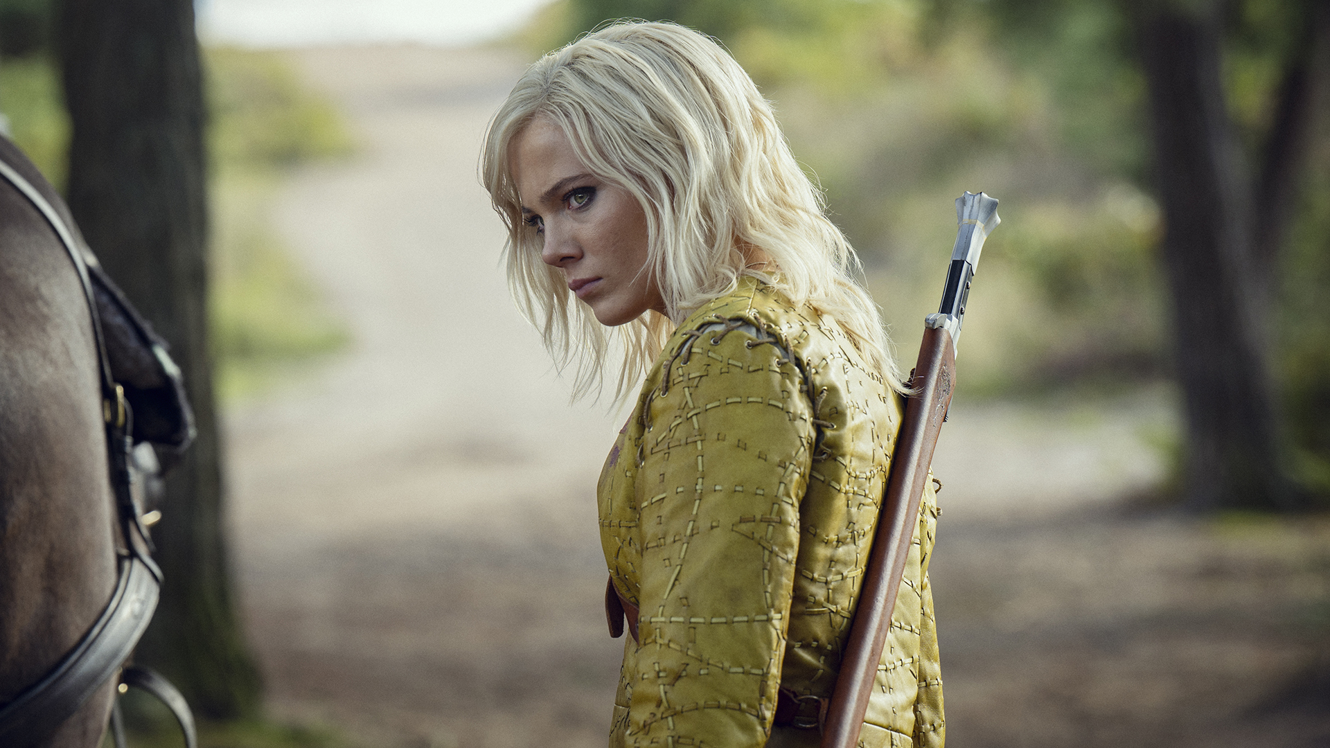 Ciri wearing a mustard yellow-colored top and a sword slung on her back in The Witcher season 4