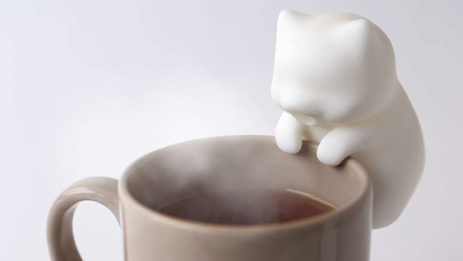 Yukai Engineering's N&amp;eacute;kojita FuFu robot cat clipped onto the side of a steaming coffee cup