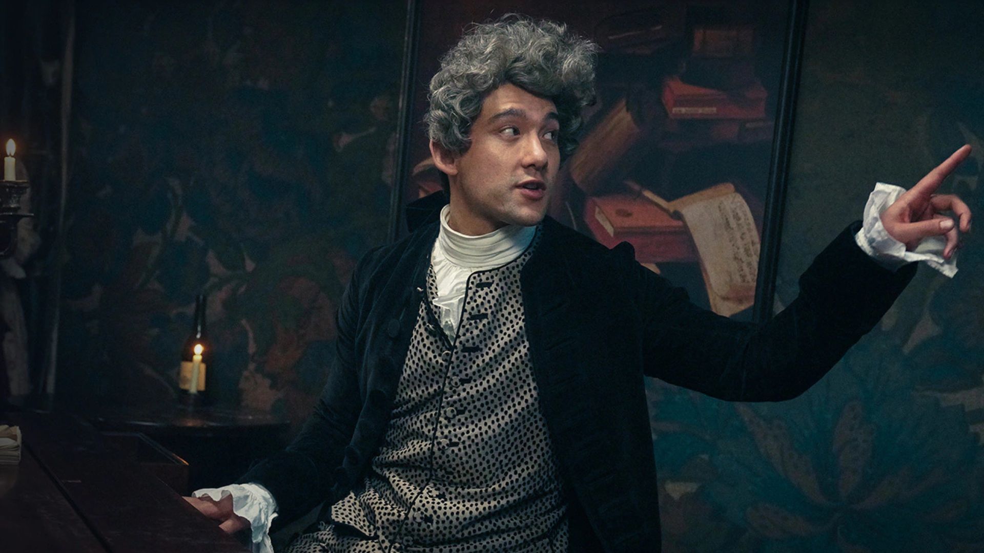 Will Sharpe sits at a piano while point a finger the other way
