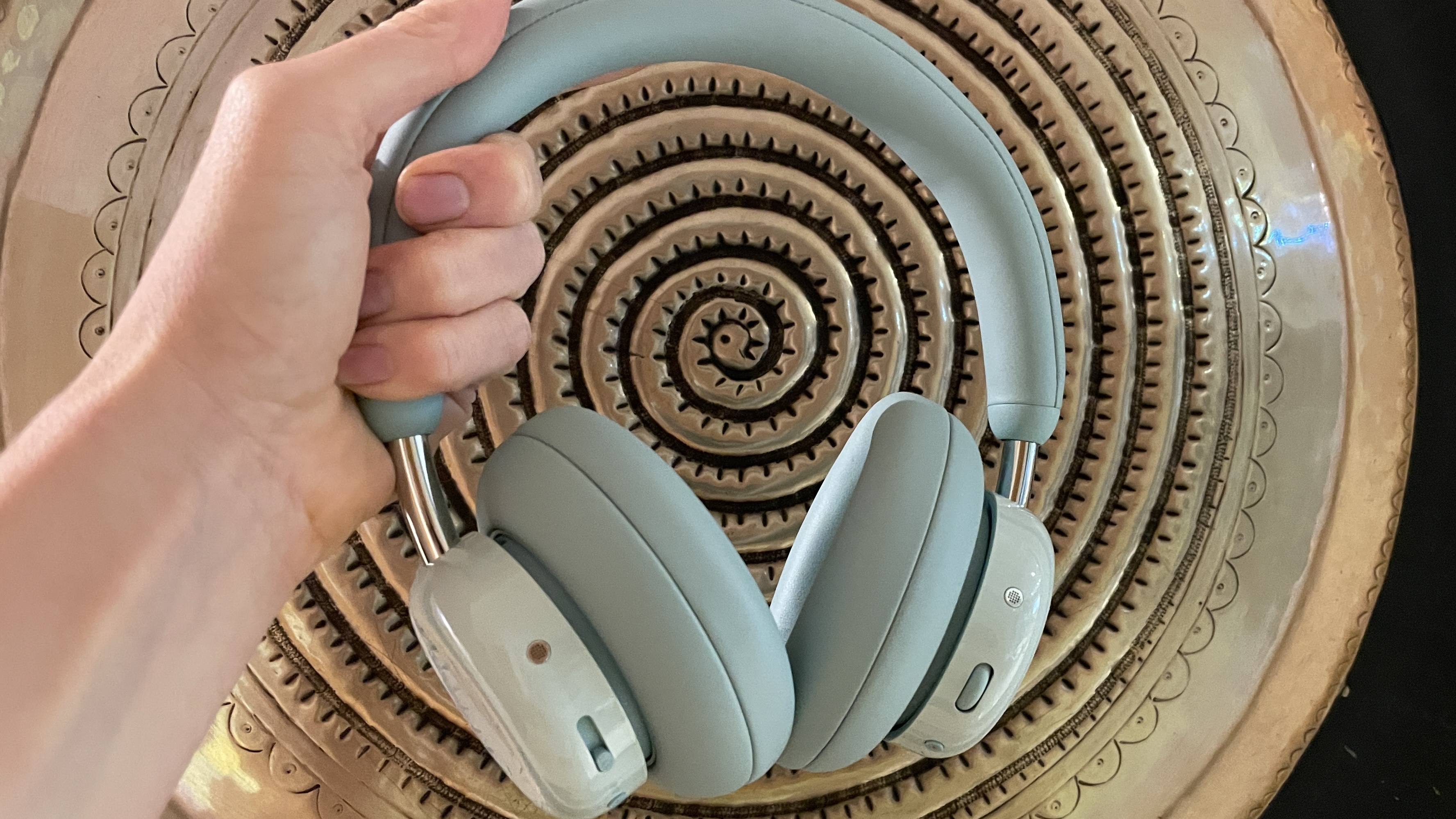CMF Headphone Pro in pistachio green held in a hand or hung on a barbell, being pushed up by a carved frog