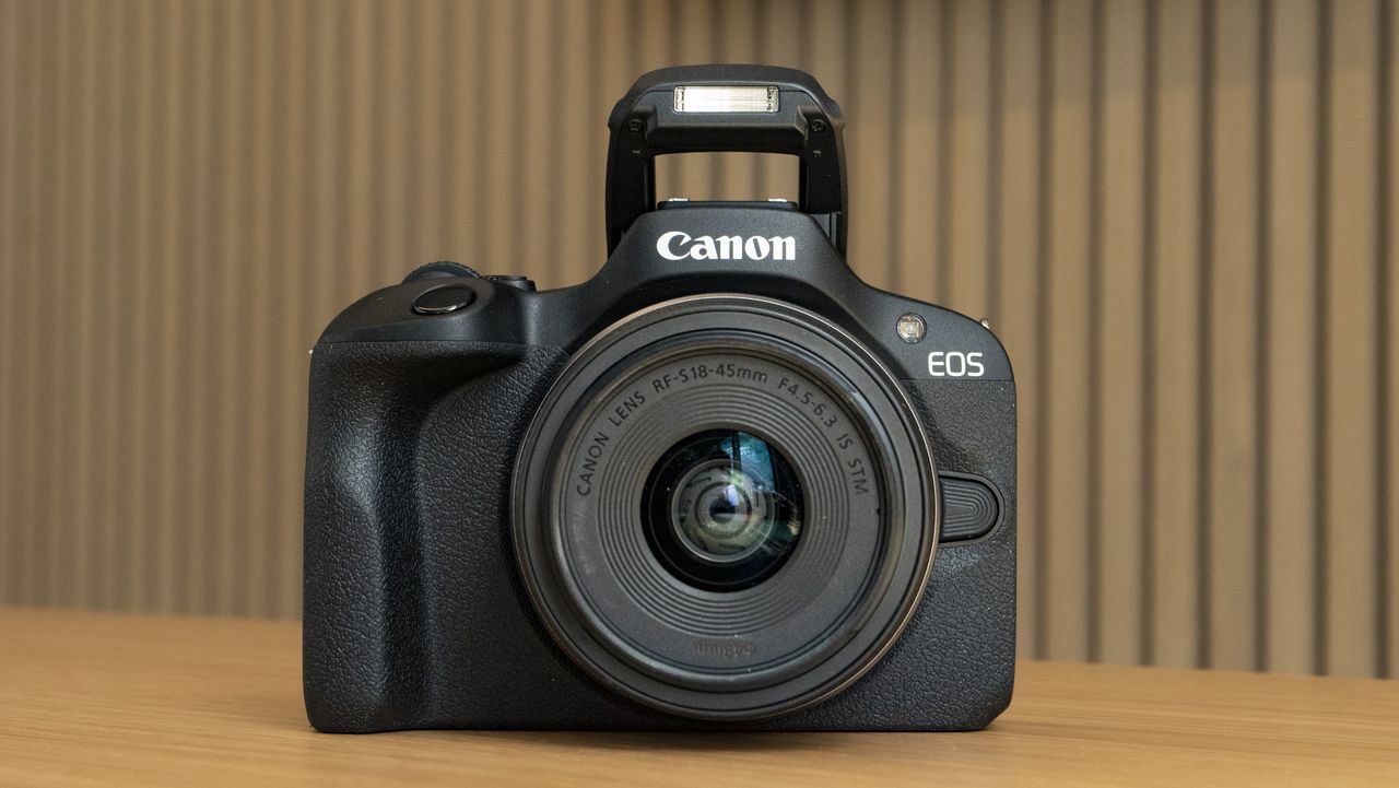 Canon EOS R100 camera on a table front with flash up