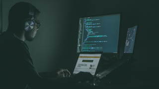 Man using a laptop and computer in a darkened home office