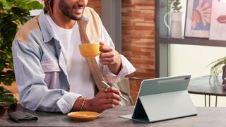 Man drinking from mug, smiling while using Samsung Galaxy Tab S7 FE