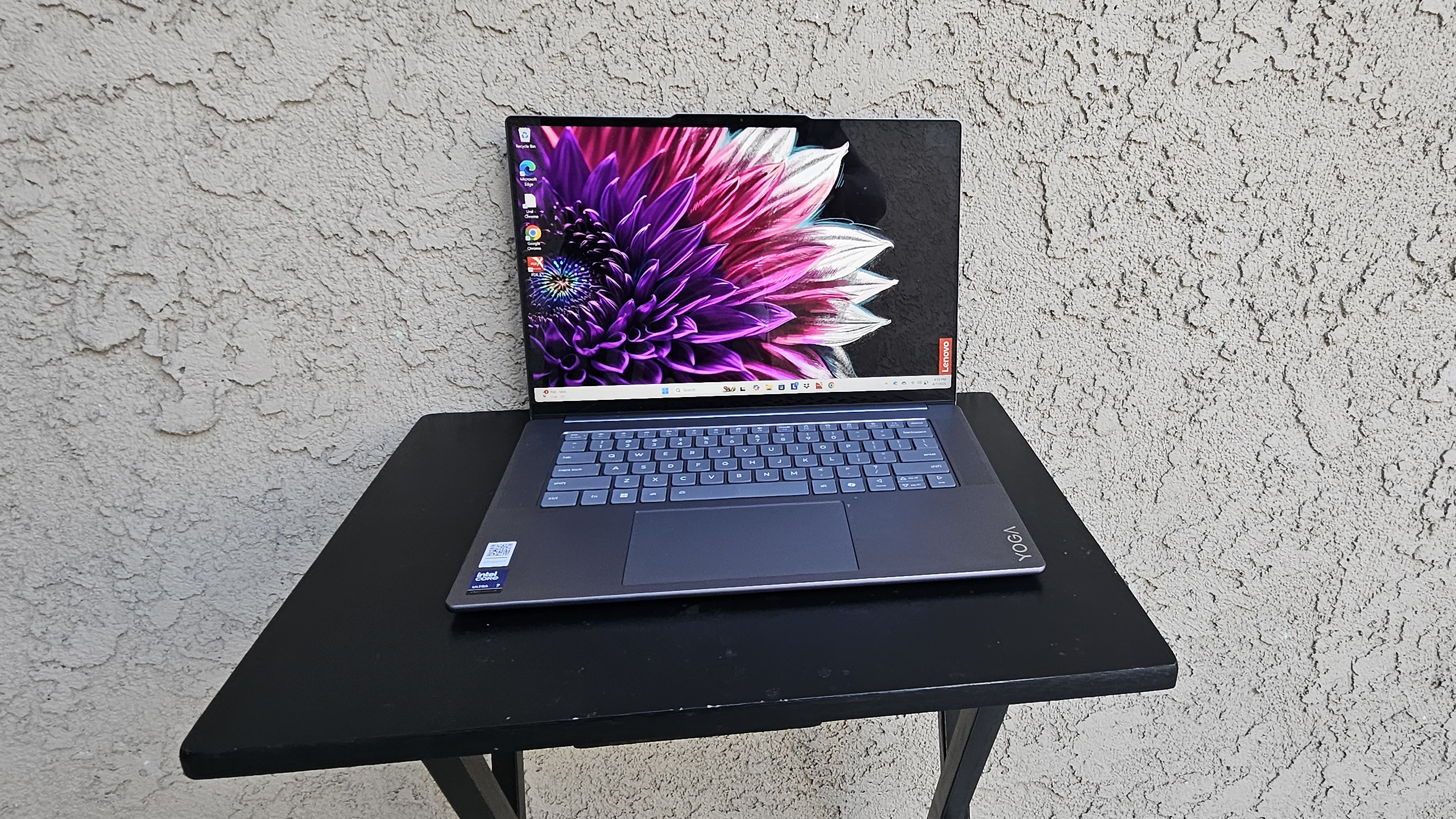 Lenovo Yoga Slim 7i Aura Edition laptop powered on and open, resting on a small black table