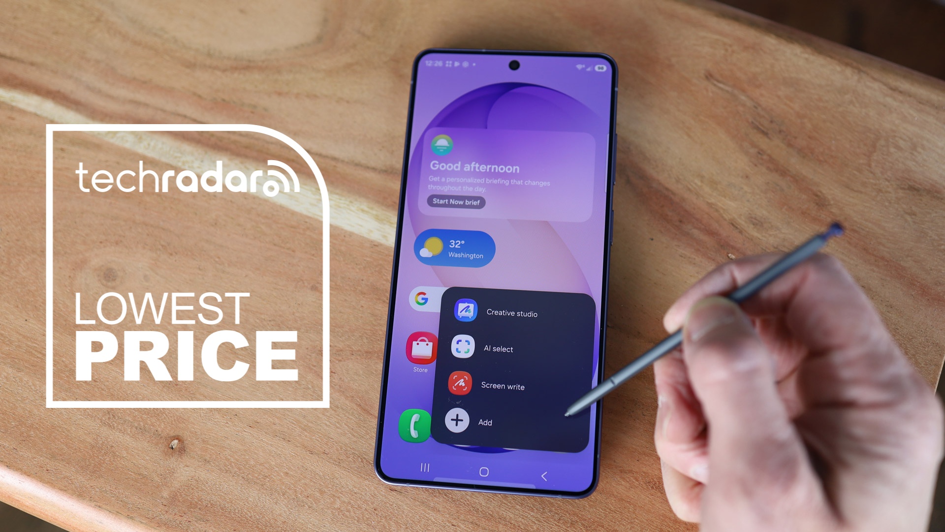 Samsung Galaxy S26 Ultra on desk top with person holding S-Pen, alongside a lowest price text overlay