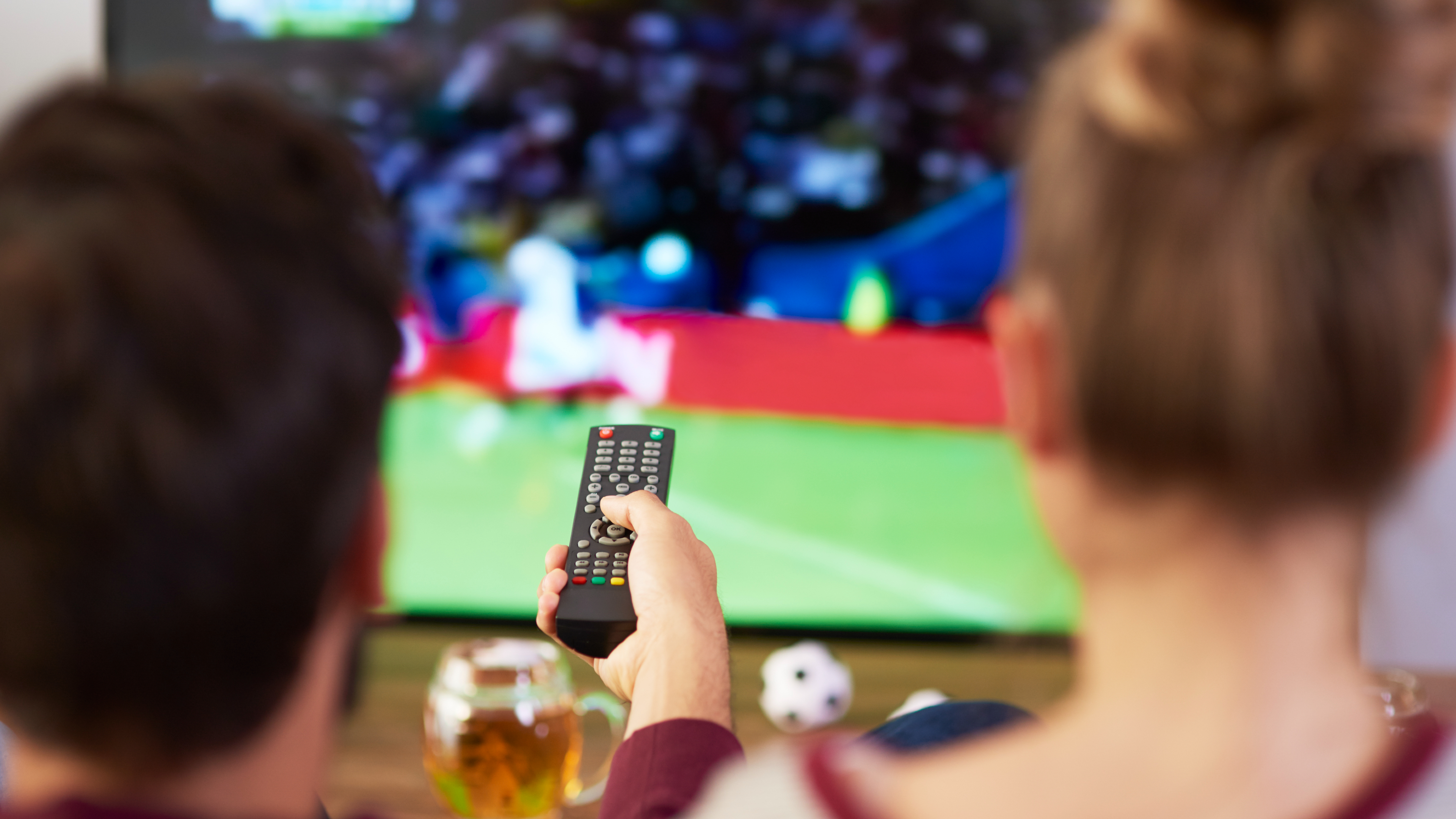 Football being watched on TV with the TV remote in focus