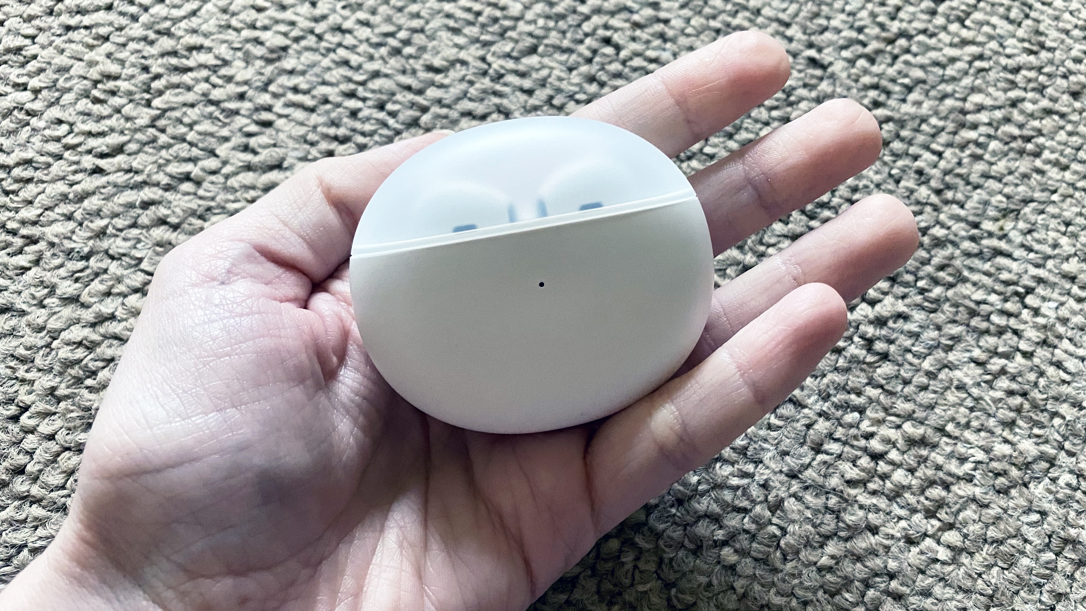a closeup of the oppo enco air in their charging case, held in an open palm