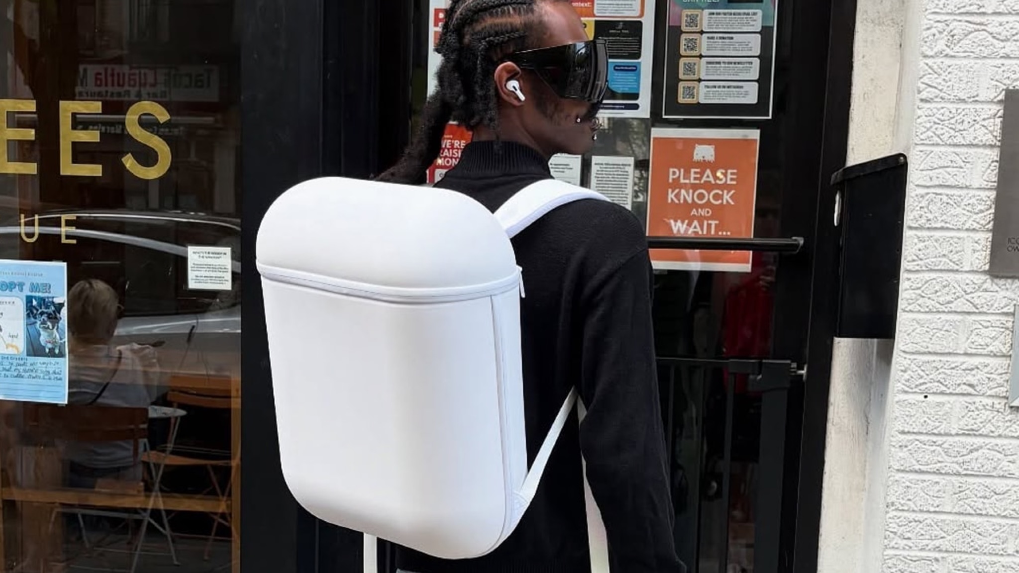 A man wearing the AIRPACK backpack in an urban street. The backpack looks like a giant AirPods charging case
