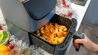 Person opening air fryer drawer with tinsel on kitchen counter