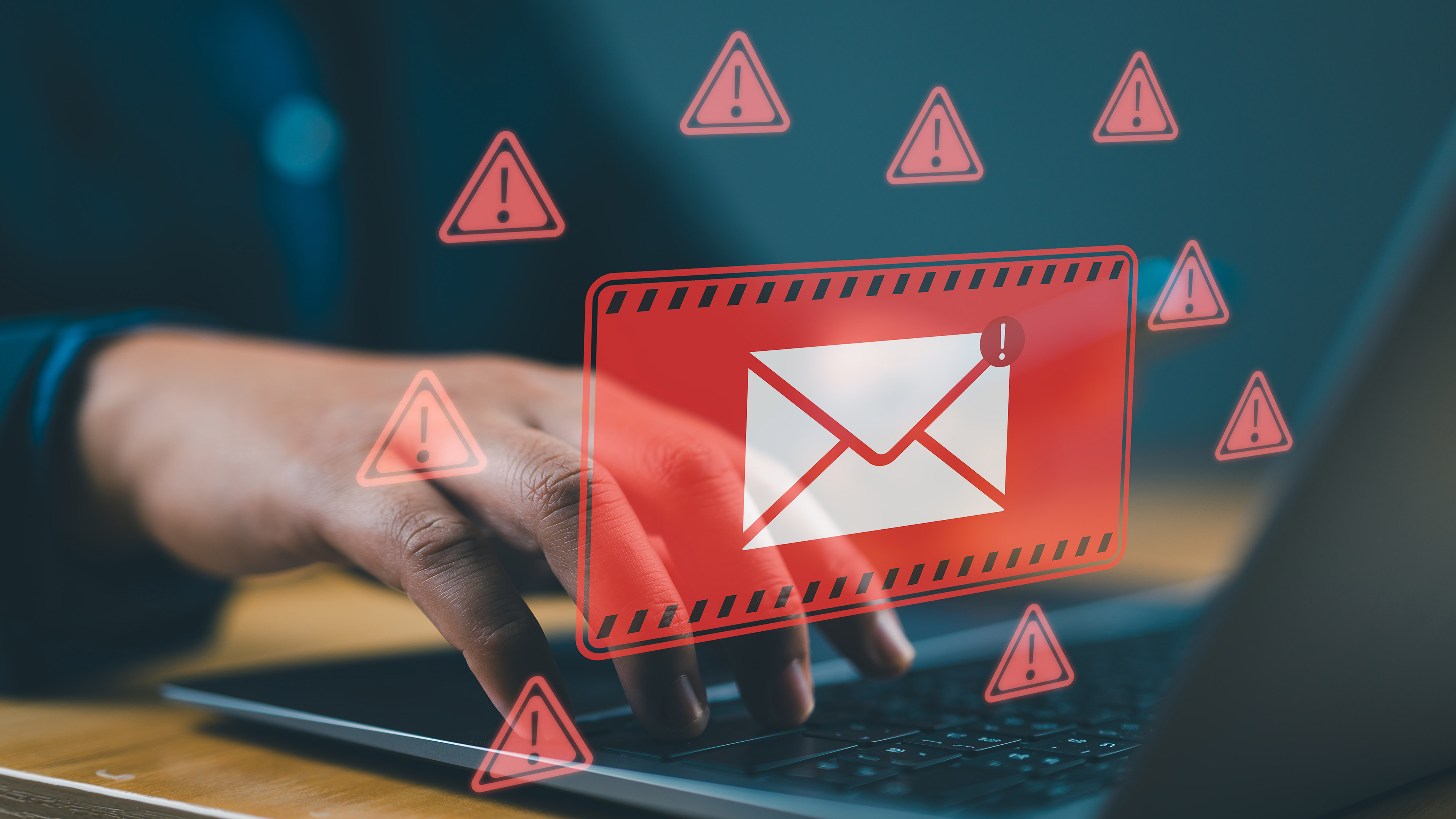 An email symbol inside a red square warning sign, surrounded by red triangles with exclamation marks inside them, superimposed on someone typing on a laptop