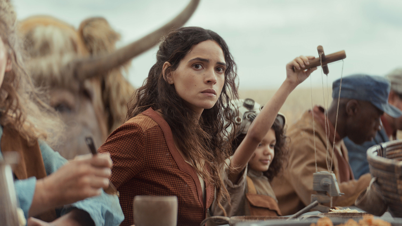 Bix Caleen sitting at a table surrounded by other villagers in Andor season 2