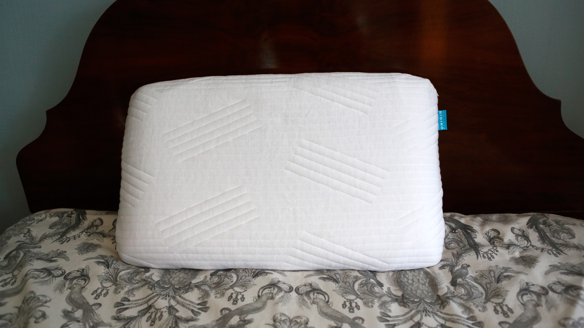 The Origin Coolmax Latex Pillow on a bed, leaning against the headboard