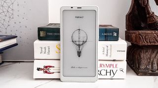 The Onyx Boox Palma 2 standing upright against a pile of books on a table