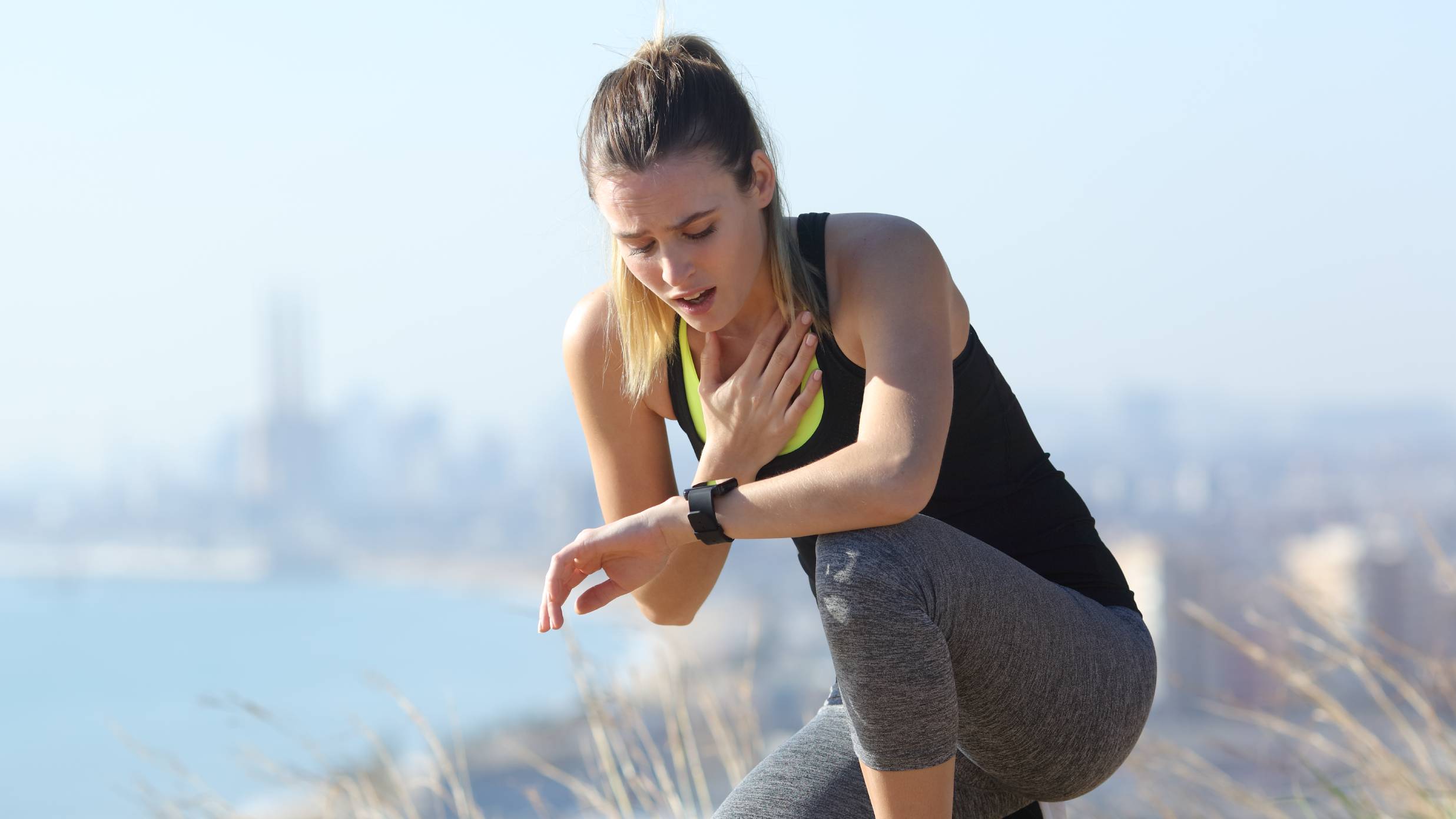 Woman with fitness tracker stopping during a sunny run, looking distressed