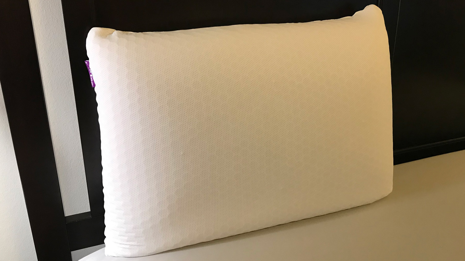 The Purple Harmony Pillow on a bed, leaning against the headboard