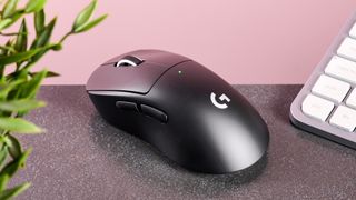 Logitech Pro X Superlight 2 Dex on table with plant and keyboard and pink wall in background