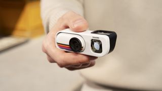 Insta360 Go 3S Retro edition, with the thumb-szied action camera slotted into the Retro Bundle's viewfinder case, held by a user