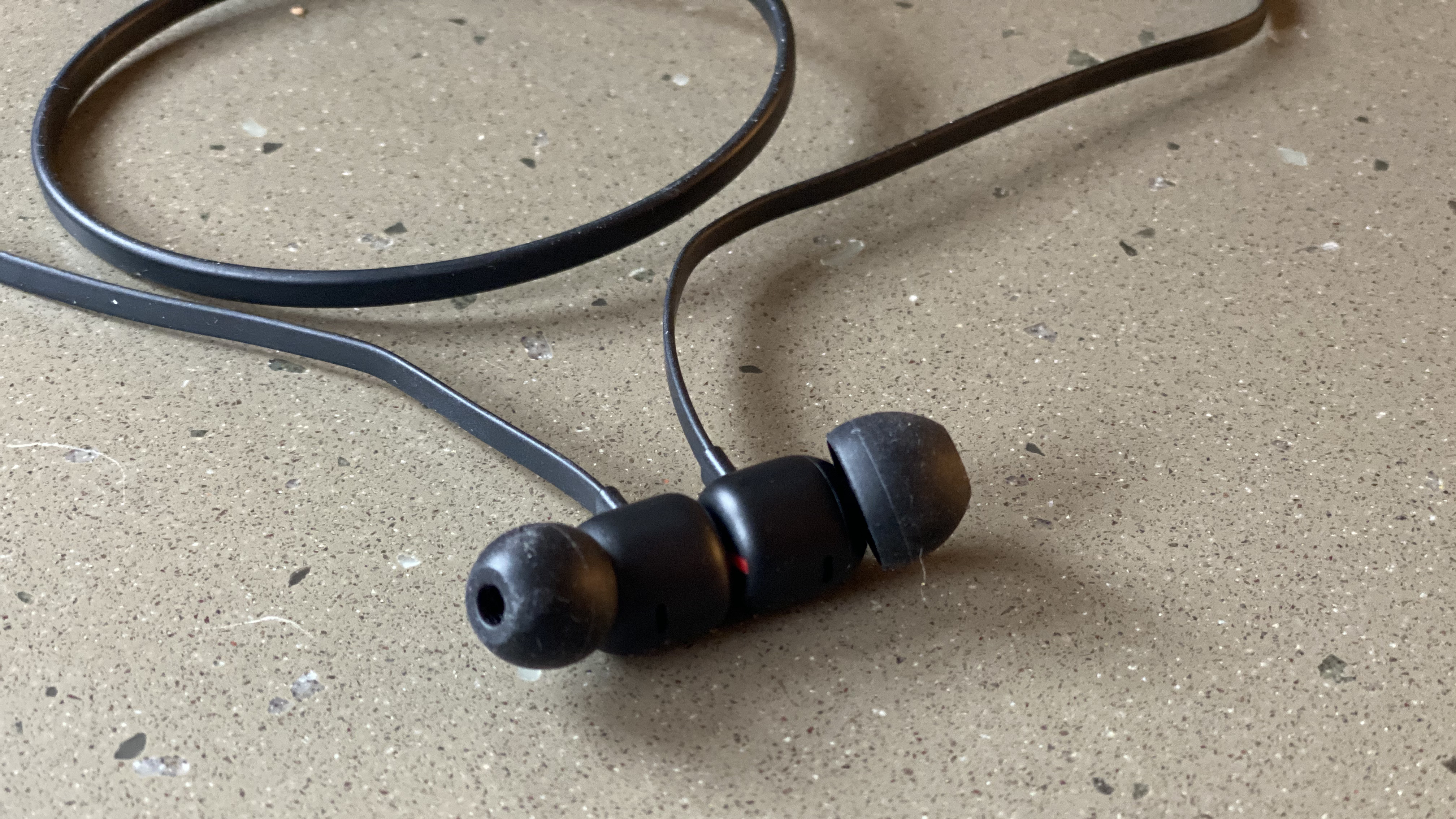 A close up of the earbuds of the Beats Flex wireless earphones in black on a marble surface