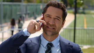 A man takes a call in front of a sports pitch