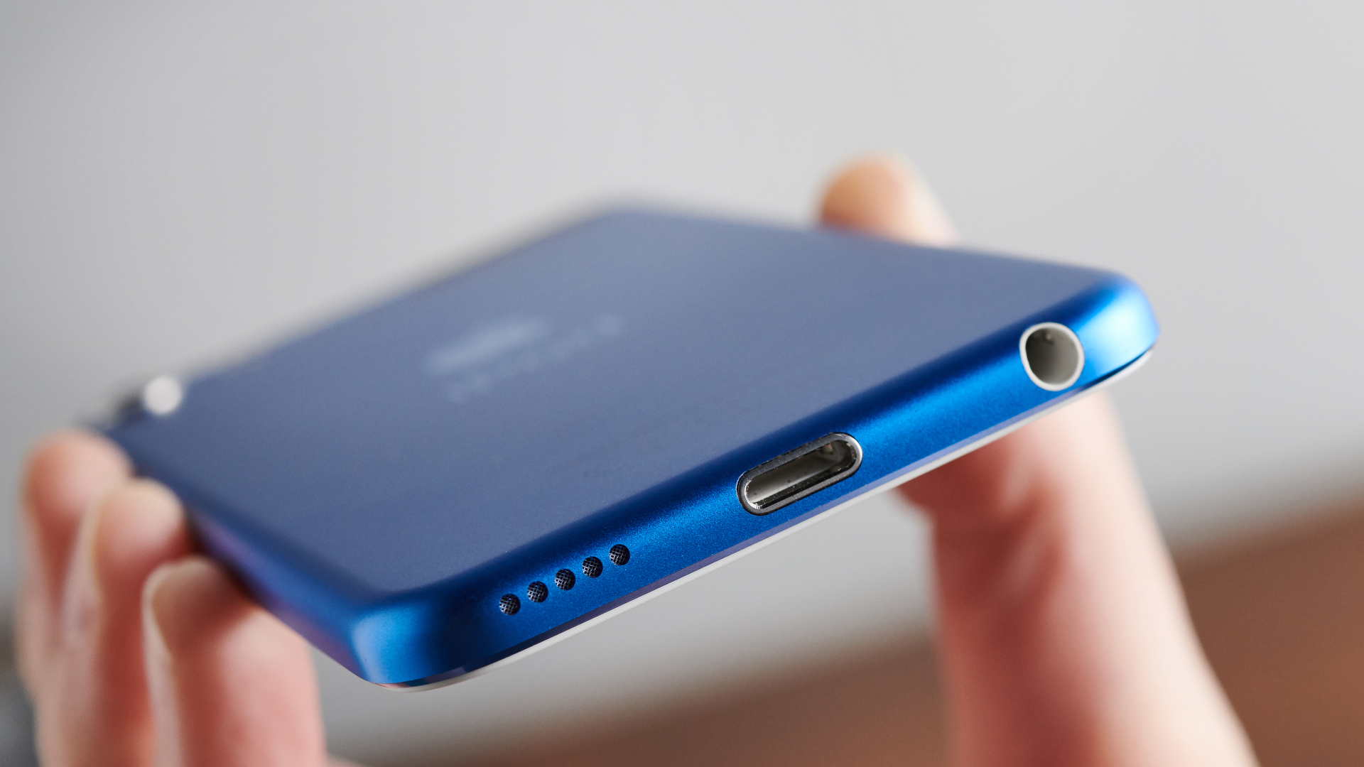 A close up of someone holding a blue iPod touch (7th generation) to the camera so you can see the ports on the bottom edge of the device.