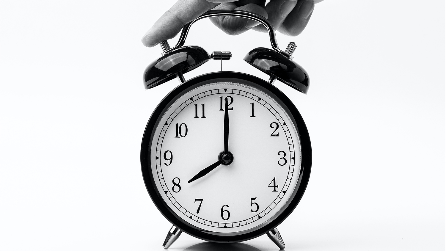 A person touches the top of a black alarm clock to stop it ringing