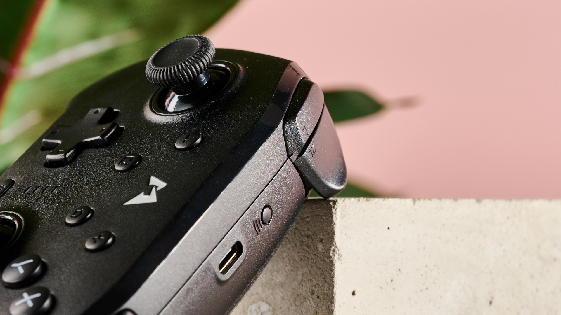 Close-up of shoulder buttons and USB-C port on Mobapad N1 HD, leaning on plinth with pink wall and plant in background