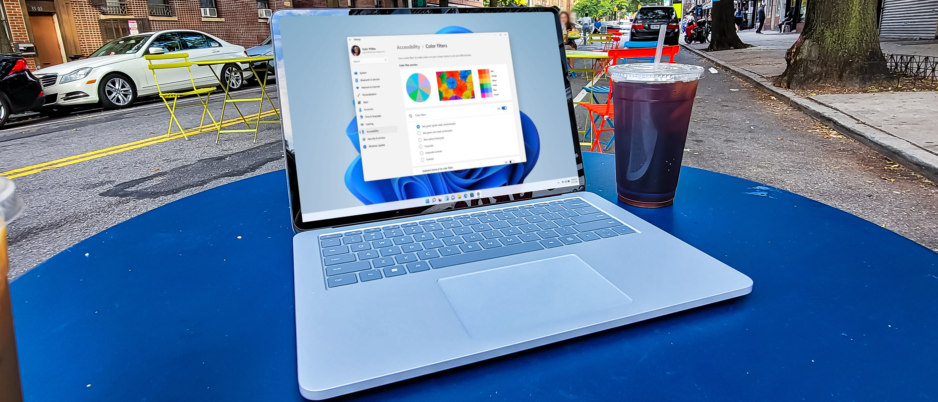 Surface Laptop Studio on a blue table, next to a cup of coffee, on a street in New York