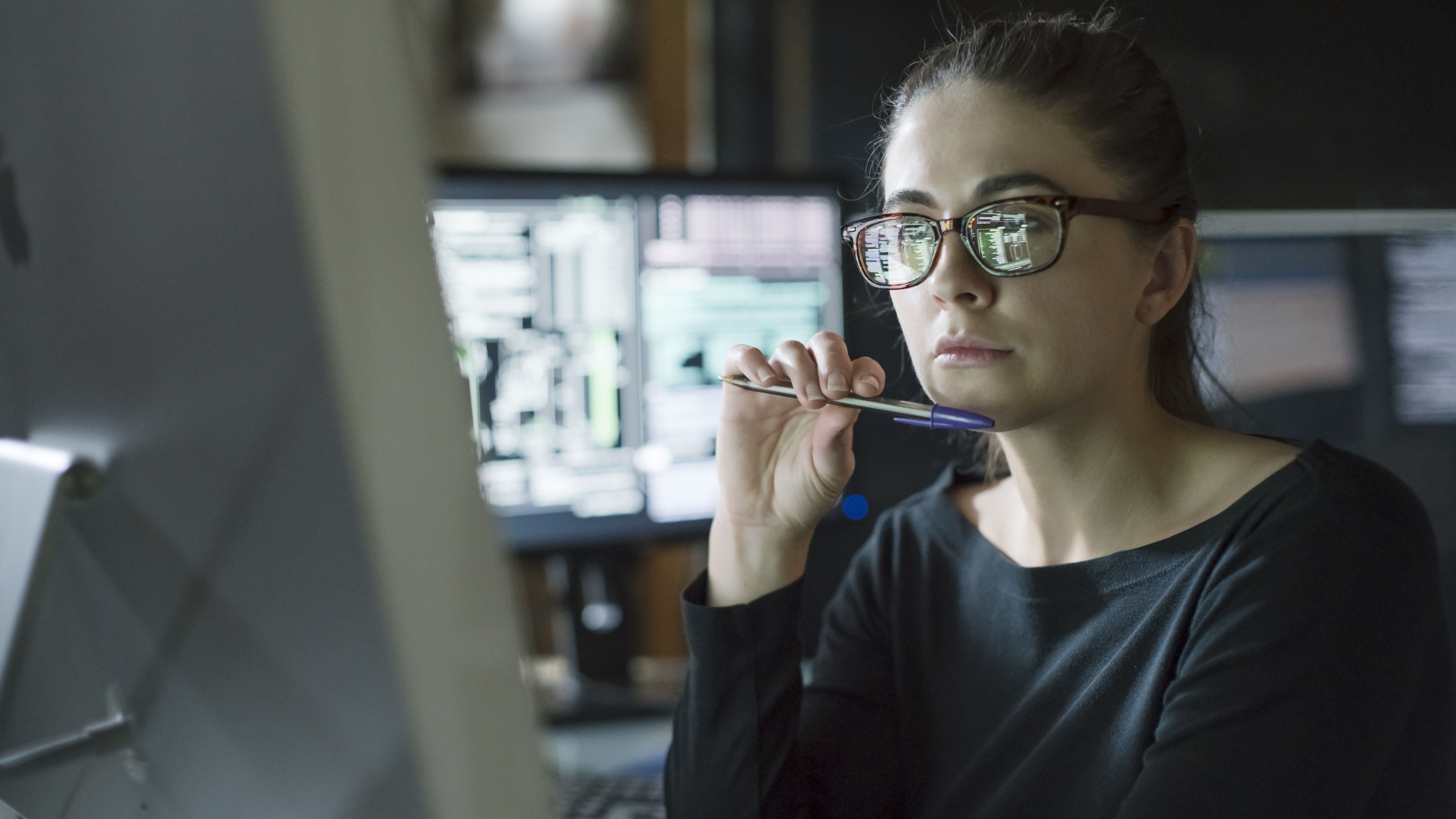 Stock photo of young woman&rsquo;s face as she contemplates one of the many computer monitors that surround her.