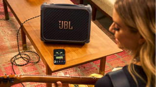 JBL BandBox Trio on a desk with a woman playing guitar next to it