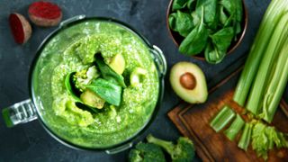 Pureeing vegetables in a blender on a kitchen countertop with avocado and celery next to the blender