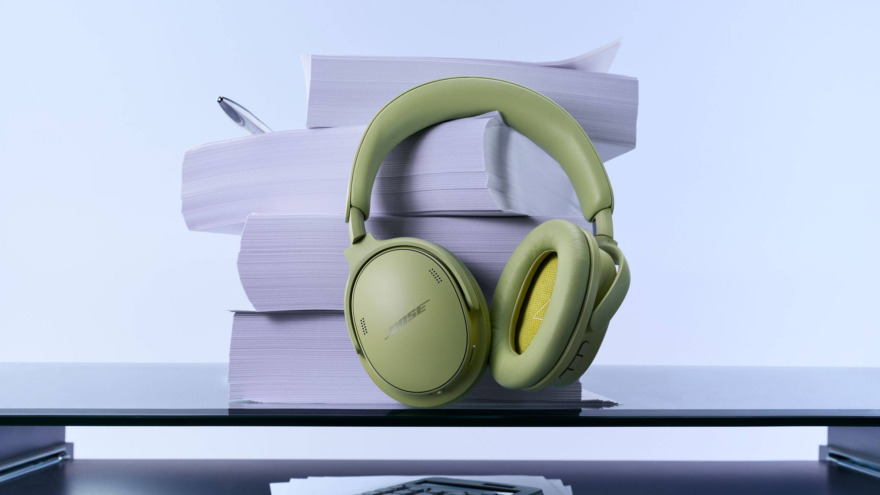 The Eucalyptus Green Bose QuietComfort Headphones (2nd Gen) on a desk, leaning on some papers.