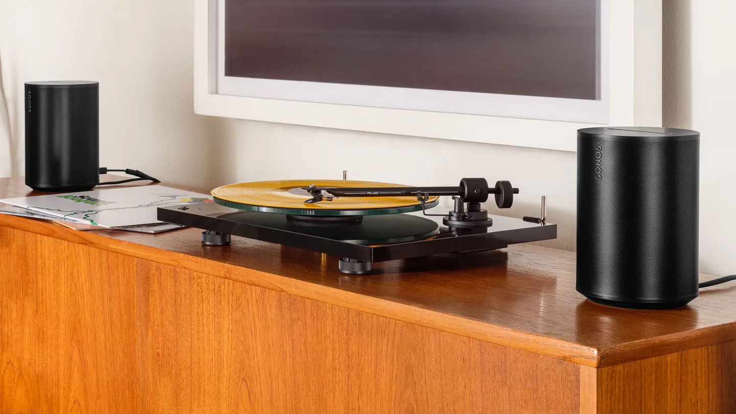 Two black speakers positioned on a wooden cabinet on either side of a record player with the edge of a TV visible at the top.