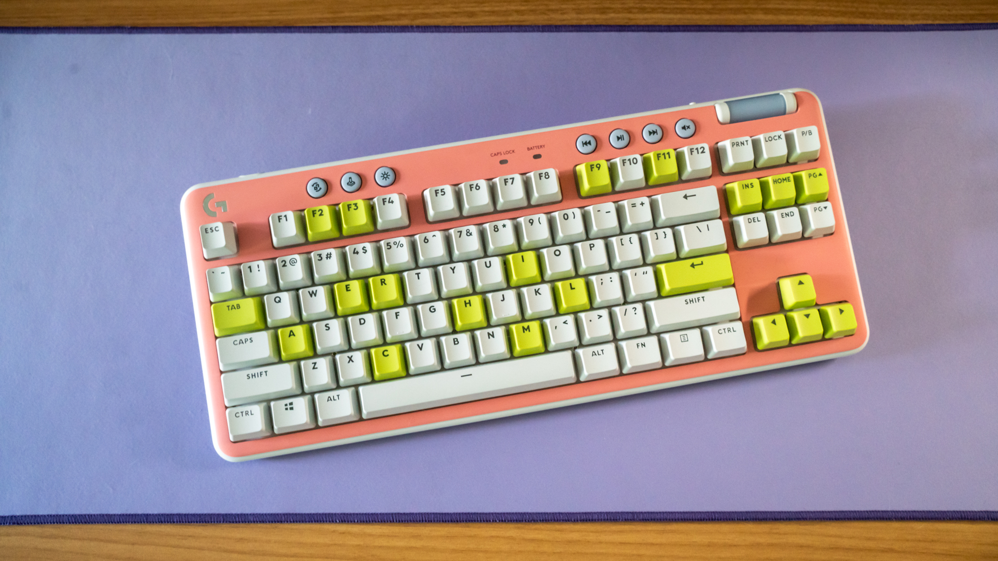 Logitech G715 TKL in its pink deck cover and white and green keys on purple Logitech desk mat
