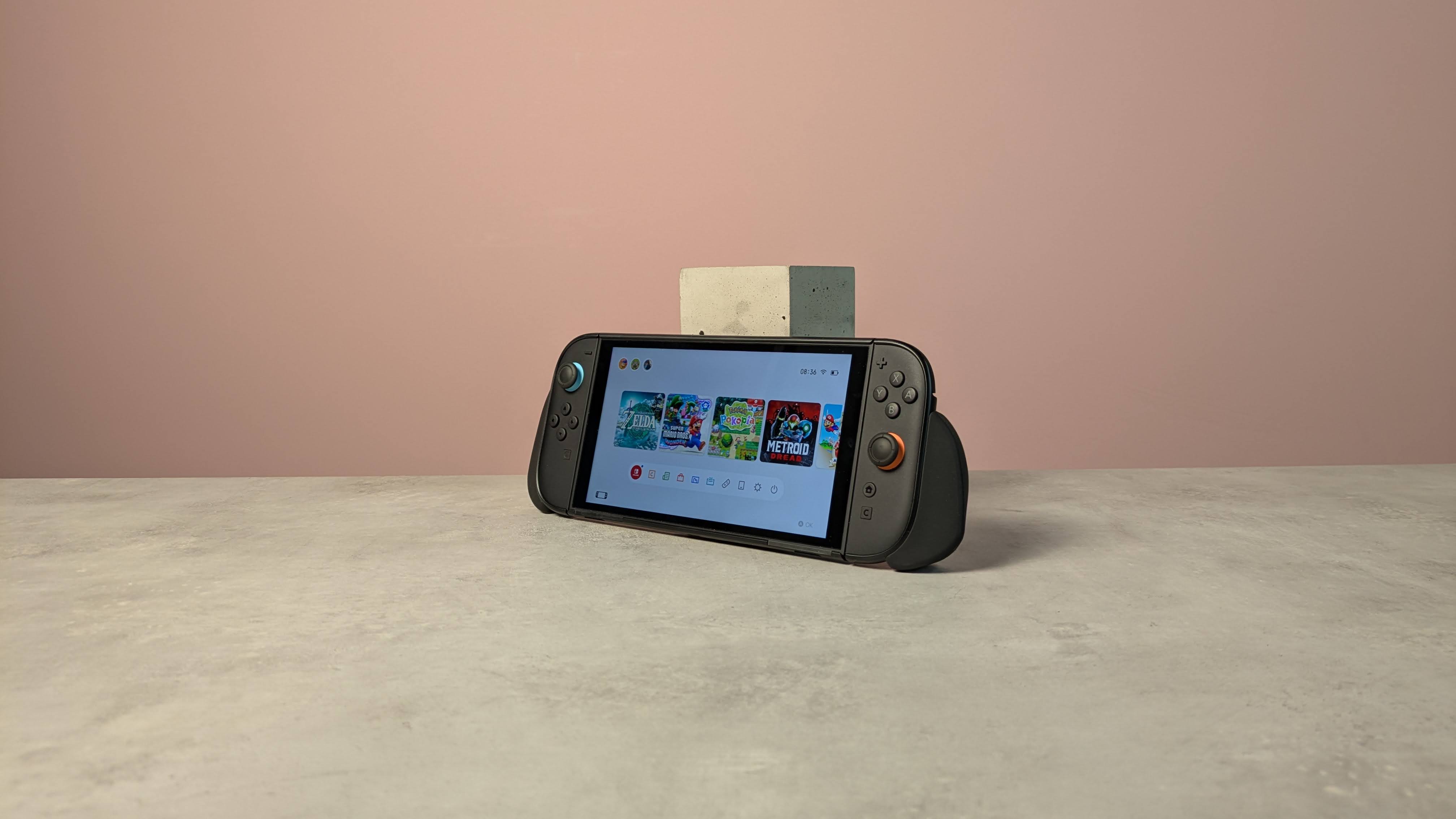 Nintendo Switch 2 leaning against plinth on desk with Genki Attack Vector attached, against a pink background
